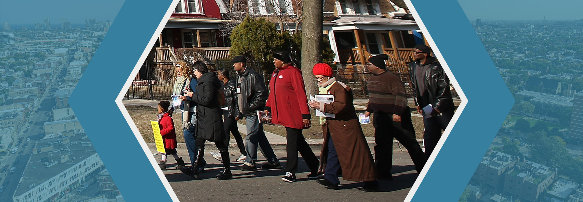 A group of people walk along a street with similar styled houses in the background.